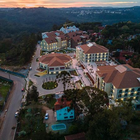 Buona Vitta Gramado Resort & Spa By Gramado Parks Zewnętrze zdjęcie The photo shows an aerial view of a hotel complex set in a hilly, wooded area. The buildings feature a mix of architectural styles with several structures, including a central round pavilion. Surrounding the buildings are well-maintained gardens and 