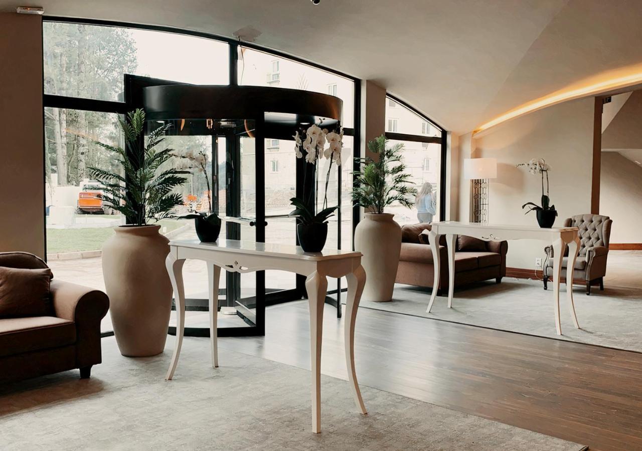 Buona Vitta Gramado Resort & Spa By Gramado Parks Zewnętrze zdjęcie The photo displays an elegant interior space, likely a hotel or a high-end lobby. In the foreground, there is a stylish table with a curved design, positioned near large glass doors leading outside. Flanking the table are two large planters with lush