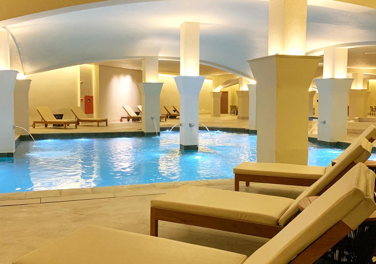 Buona Vitta Gramado Resort & Spa By Gramado Parks Zewnętrze zdjęcie The photo shows an indoor spa or relaxation area with a tranquil atmosphere. There is a large swimming pool with clear blue water, illuminated by soft lighting. Surrounding the pool are several comfortable lounge chairs. The architecture features ele