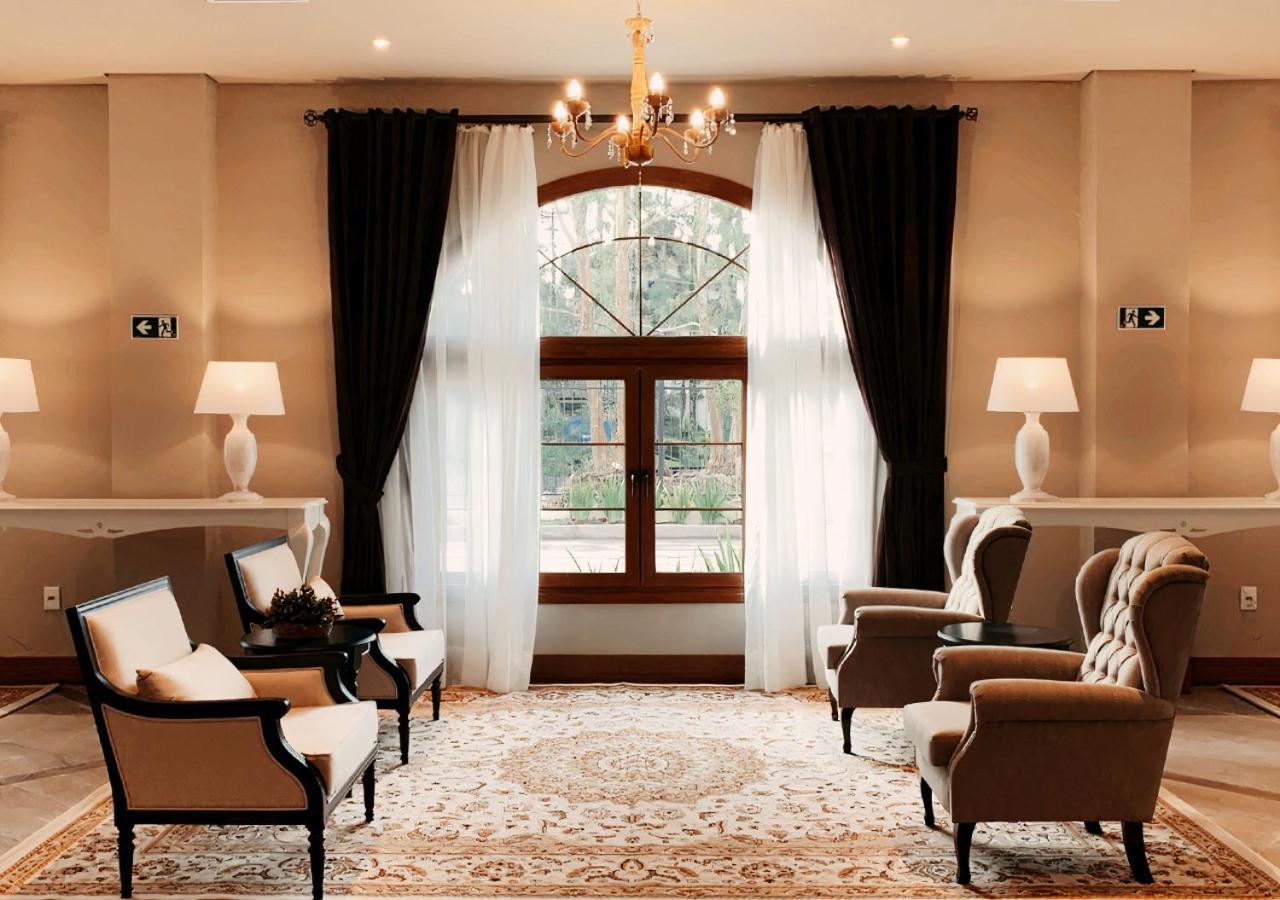 Buona Vitta Gramado Resort & Spa By Gramado Parks Zewnętrze zdjęcie The photo shows an elegantly styled living room. There are two armchairs and a sofa arranged comfortably around an intricate area rug. Large windows are adorned with sheer white curtains and dark curtains, allowing natural light to fill the space. A 
