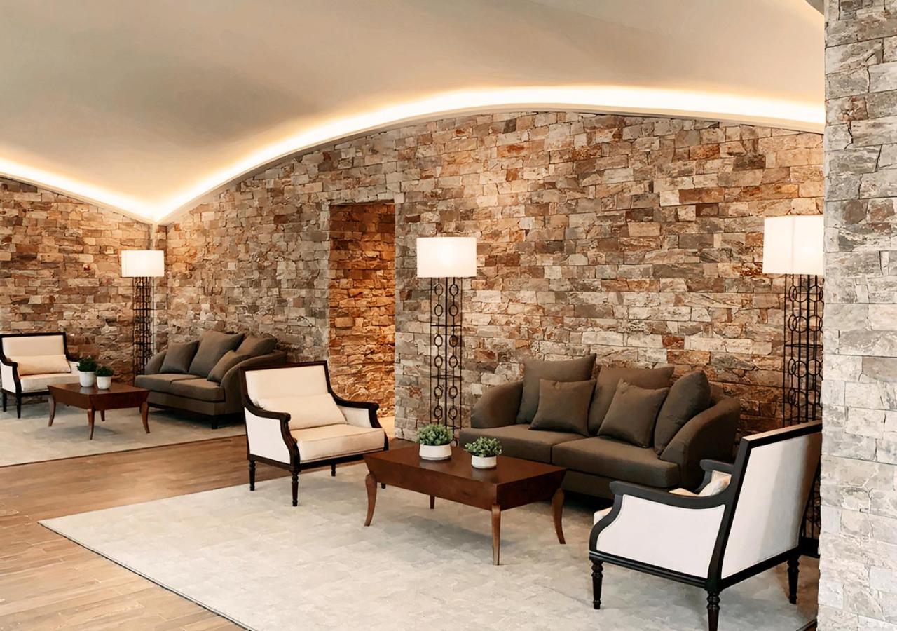 Buona Vitta Gramado Resort & Spa By Gramado Parks Zewnętrze zdjęcie The photo shows a stylish and modern lounge area. The walls are made of natural stone, creating a warm and inviting atmosphere. There are two comfortable sofas in a muted gray color arranged around a wooden coffee table. Flanking the sofas are elegan