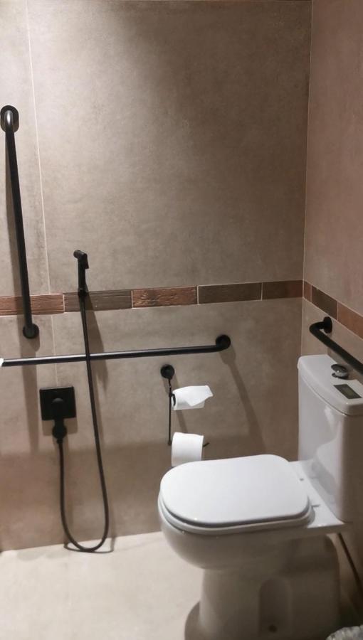 Buona Vitta Gramado Resort & Spa By Gramado Parks Zewnętrze zdjęcie The photo shows a bathroom equipped with grab bars for accessibility. The walls are tiled in a neutral color, and there is a toilet on the right side of the image. Two rolls of toilet paper are positioned near the toilet, and there are additional ins