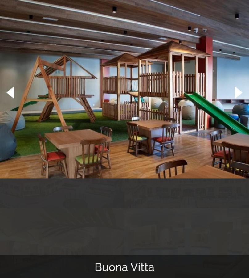 Buona Vitta Gramado Resort & Spa By Gramado Parks Zewnętrze zdjęcie The photo shows a play area designed for children, featuring a wooden play structure with slides and climbing areas. In the foreground, there are several small wooden tables and chairs arranged for seating. The floor is covered with green turf, resem