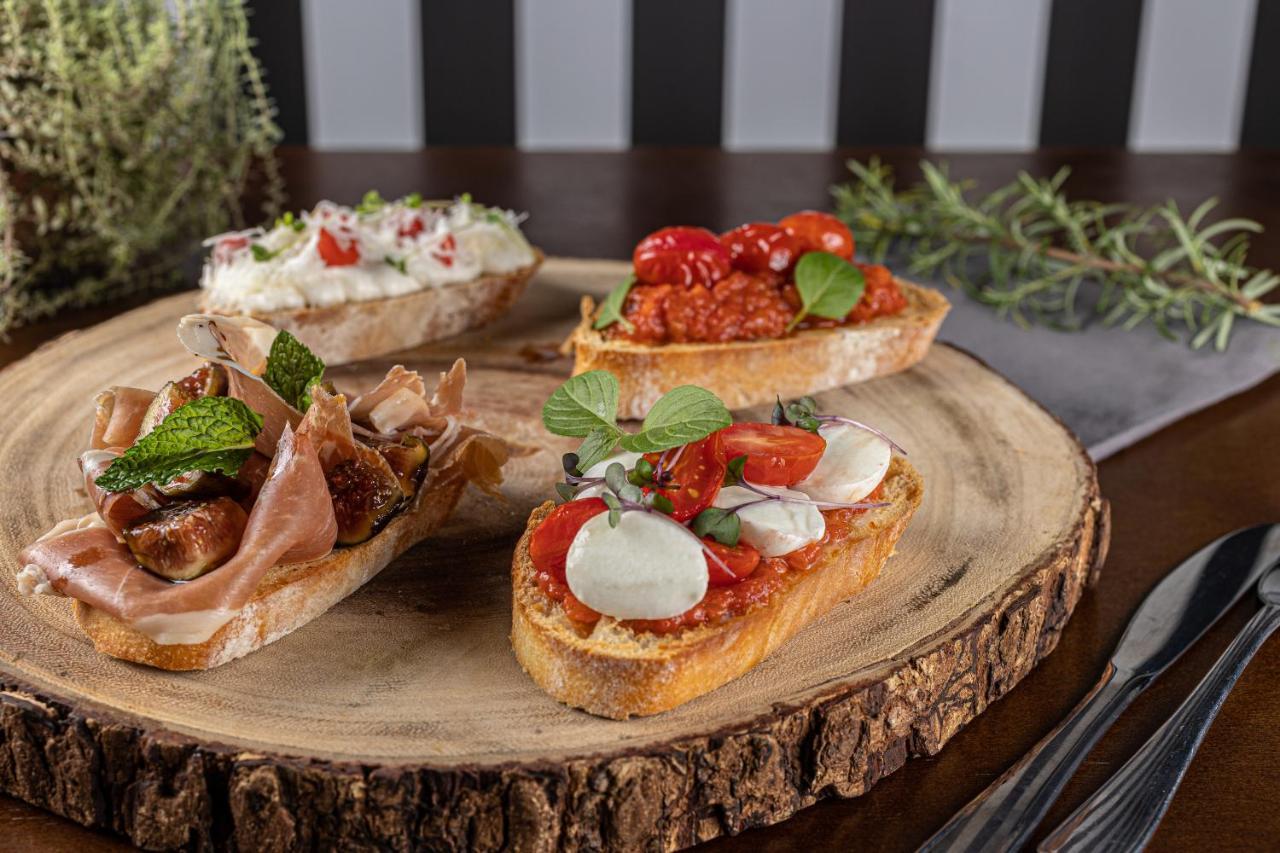 Buona Vitta Gramado Resort & Spa By Gramado Parks Zewnętrze zdjęcie The photo displays a wooden serving platter featuring four different types of bruschetta. Each piece of bruschetta is topped with various ingredients:

1. The top left has a creamy spread, possibly cheese or ricotta, garnished with fresh herbs and sm