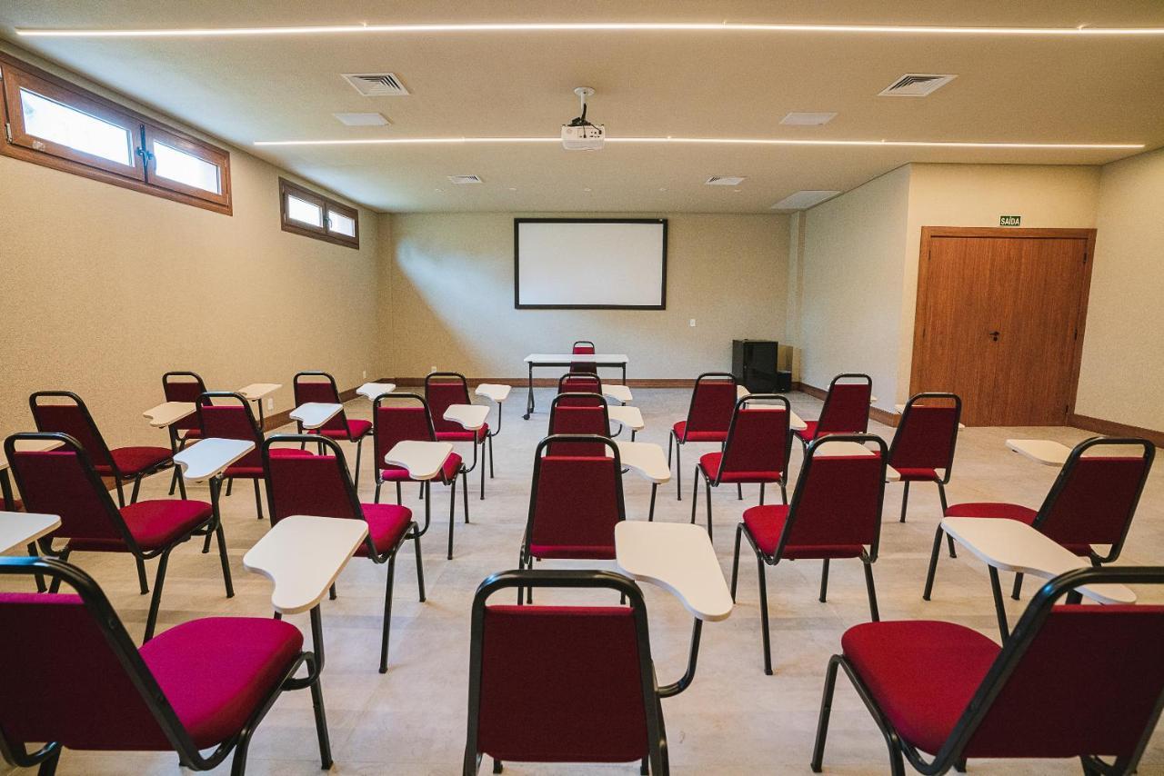 Buona Vitta Gramado Resort & Spa By Gramado Parks Zewnętrze zdjęcie The photo shows a classroom or meeting room set up for a presentation or lecture. It features several rows of red chairs, each with a small writing surface attached. There is a blank screen mounted on the wall at the front of the room, likely for dis
