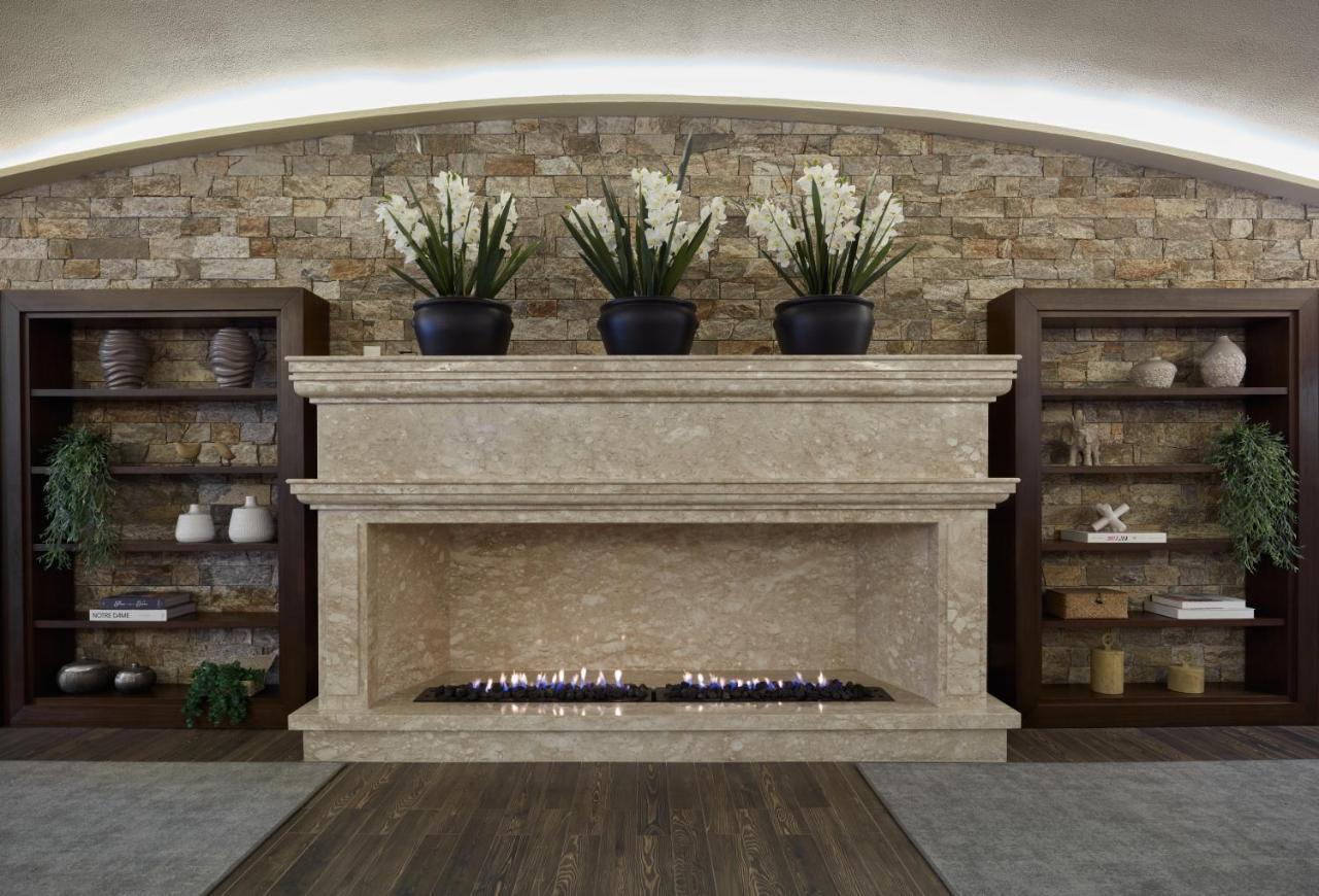 Buona Vitta Gramado Resort & Spa By Gramado Parks Zewnętrze zdjęcie The photo shows a modern fireplace design built into a wall with a textured stone background. The fireplace is made of a light-colored stone and features a long, narrow gas flame visible at the bottom. Above the fireplace, there are two large potted 