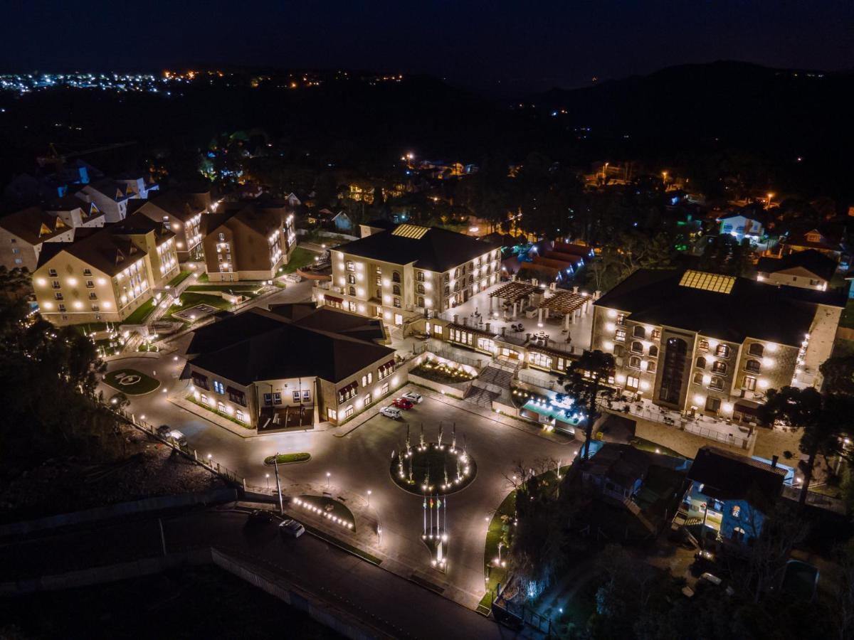 Buona Vitta Gramado Resort & Spa By Gramado Parks Zewnętrze zdjęcie The photo shows a beautifully lit resort or hotel complex taken at night. The buildings are well-illuminated, highlighting their architecture. There is a circular area with a fountain at the center, surrounded by pathways that connect various parts o
