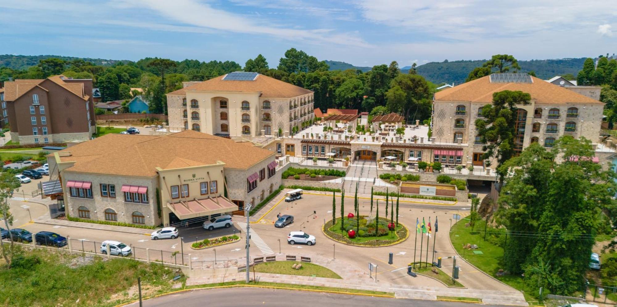 Buona Vitta Gramado Resort & Spa By Gramado Parks Zewnętrze zdjęcie The photo shows an aerial view of a hotel complex surrounded by lush greenery. The buildings are designed with beige and light-colored facades, featuring multiple stories and a spacious layout. In the foreground, there is a circular road with several