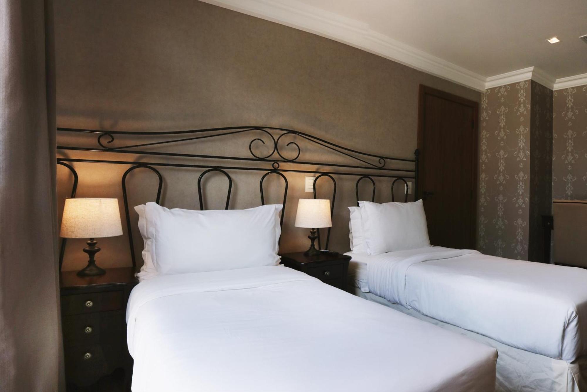 Buona Vitta Gramado Resort & Spa By Gramado Parks Zewnętrze zdjęcie The photo shows a neatly arranged hotel room featuring two single beds with white bedding. The beds have decorative metal headboards, and there are bedside tables on either side with lamps. The room's walls have a subtle design, and there is a door v