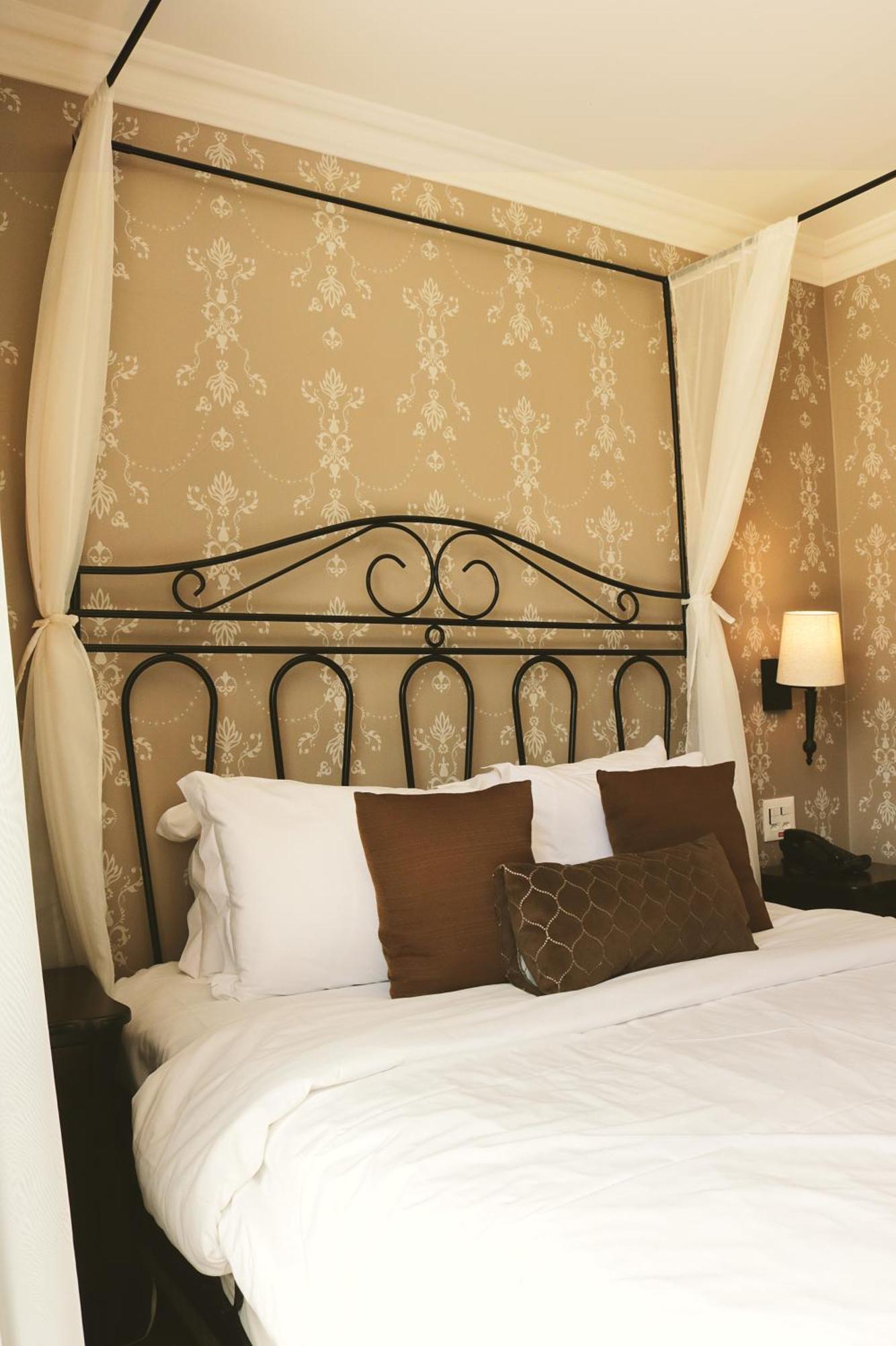 Buona Vitta Gramado Resort & Spa By Gramado Parks Zewnętrze zdjęcie The photo shows a cozy bedroom setup featuring a decorative metal bed frame with a scroll design as the headboard. The bed is adorned with several white pillows and two brown decorative cushions. The wall behind the bed is covered with a light-colore