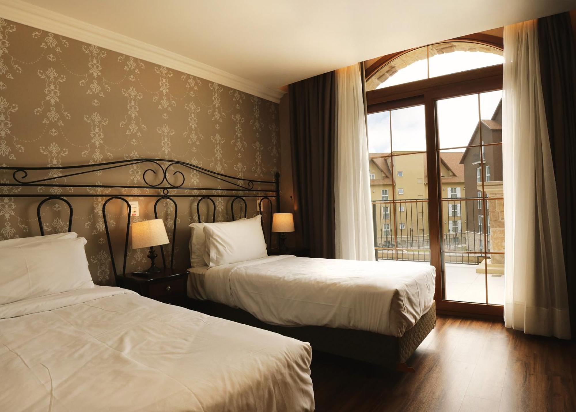 Buona Vitta Gramado Resort & Spa By Gramado Parks Zewnętrze zdjęcie The photo shows a well-decorated hotel room featuring two beds. One bed is larger, likely a double bed, while the other is a single bed. The walls are adorned with a floral pattern, and there are bedside lamps next to the larger bed. Large windows wi