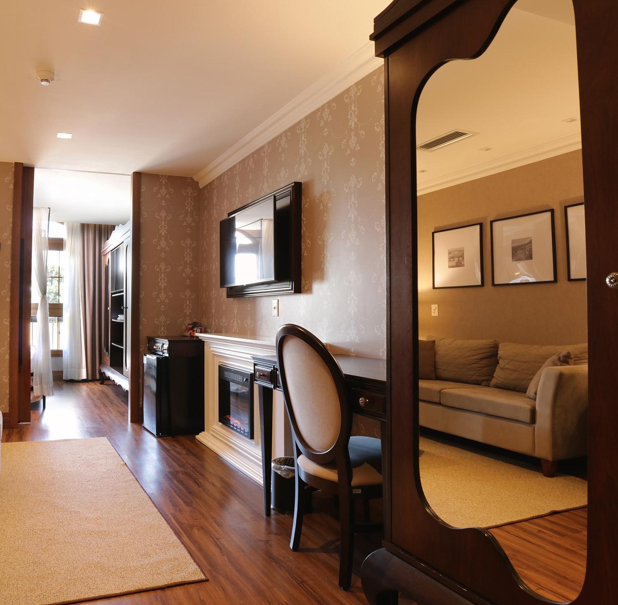 Buona Vitta Gramado Resort & Spa By Gramado Parks Zewnętrze zdjęcie The photo shows a well-decorated room that appears to be a living area or a hotel suite. In the foreground, there is a round chair and a desk. A large mirror reflects the living space, creating a sense of spaciousness. 

On the wall is a flat-screen 