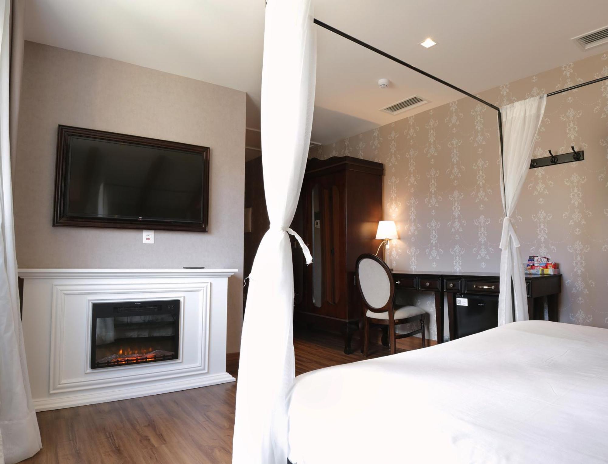 Buona Vitta Gramado Resort & Spa By Gramado Parks Zewnętrze zdjęcie The photo shows a cozy hotel room with elegant decor. There is a white bed with a canopy, and a modern television mounted on the wall across from it. To the side, a fireplace is built into a white mantel, adding a warm touch to the space. There's a w